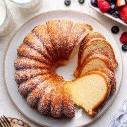 A partially sliced cream cheese pound cake on a large plate next to fresh berries.