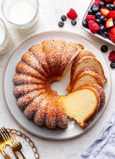 A partially sliced cream cheese pound cake on a large plate next to fresh berries.