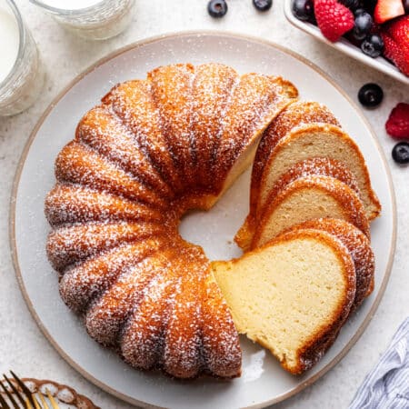 A partially sliced cream cheese pound cake on a large plate next to fresh berries.