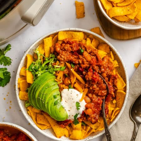 Frito chili pie topped with sour cream and sliced avocado in a dish.