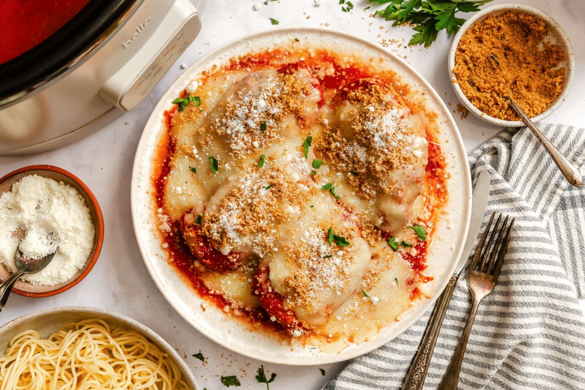 A plate of chicken parmesan next to a dish of grated parmesan and a dish of breadcrumbs. 
