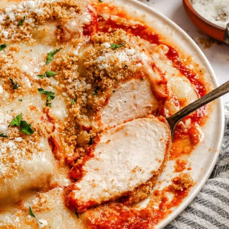 A partially sliced piece of chicken parmesan on a plate.