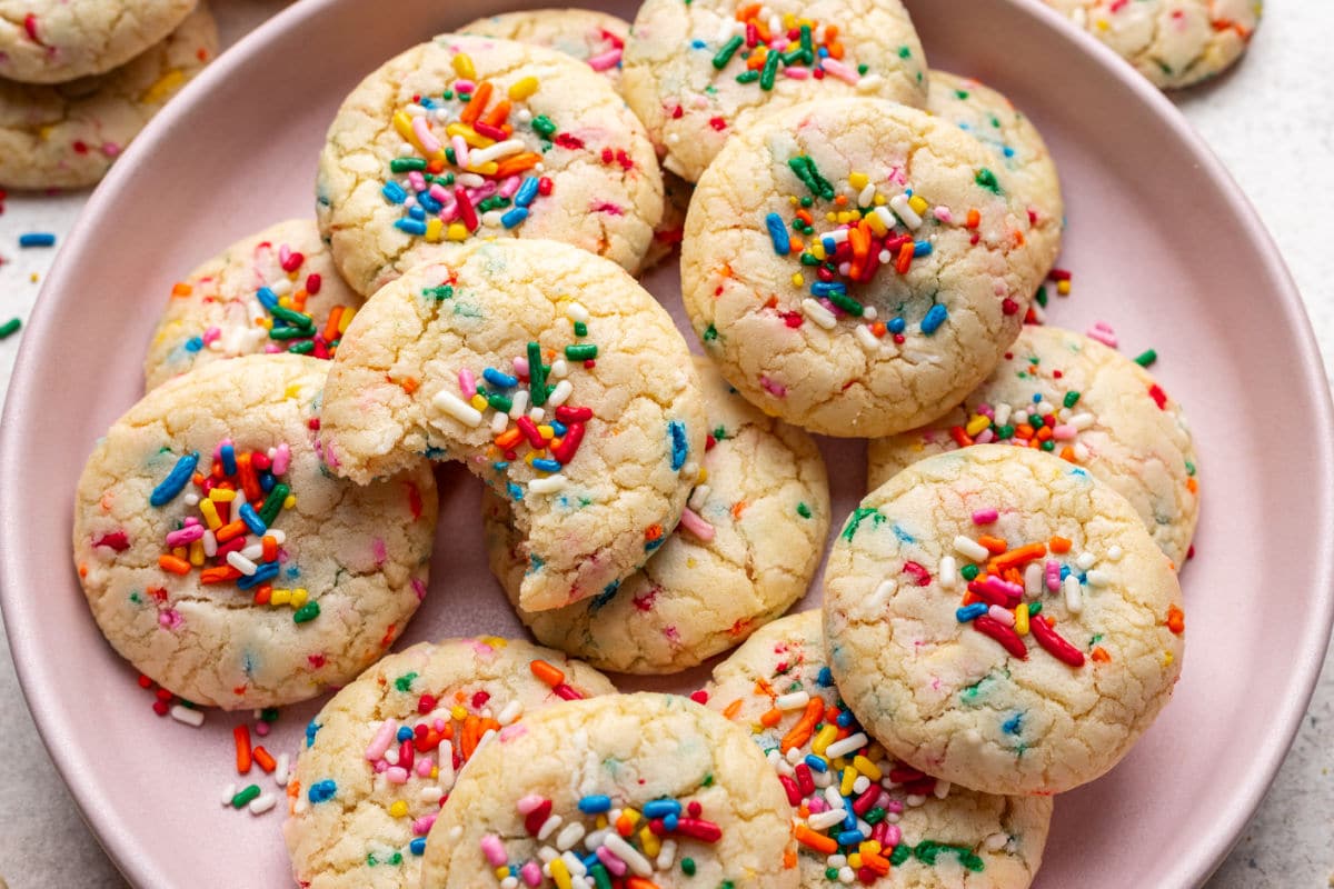 A cookie with a bite missing on top of overlapping cookies on a pink platter.