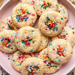 A pink plate with overlapping sprinkle cookies on it.