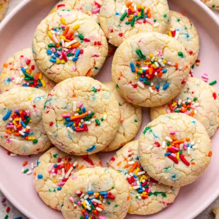 A pink plate with overlapping sprinkle cookies on it.