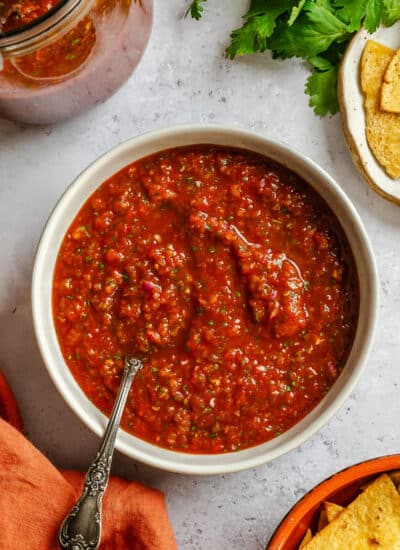 A dish of blender salsa next to a bowl of chips.