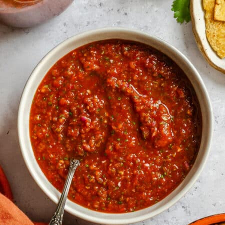 A dish of blender salsa next to a bowl of chips.