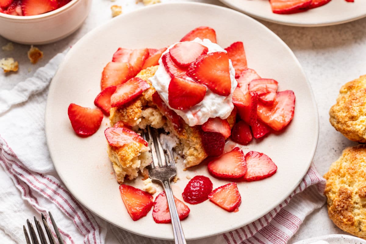 Strawberry shortcake with a fork taking a bite on a plate. 