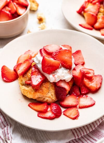 A plate with strawberry shortcake on it next to a dish of strawberries.