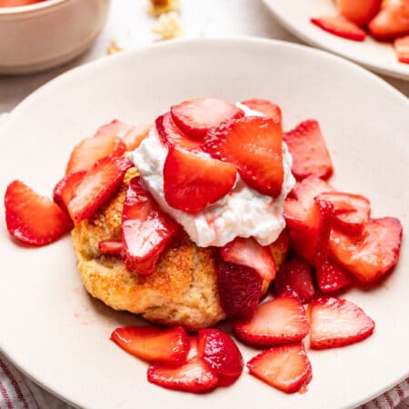 A plate with strawberry shortcake on it next to a dish of strawberries.