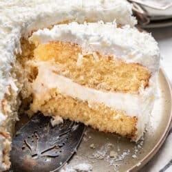 A slice of coconut layer cake next to the cake on a platter.