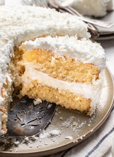 A slice of coconut layer cake next to the cake on a platter.