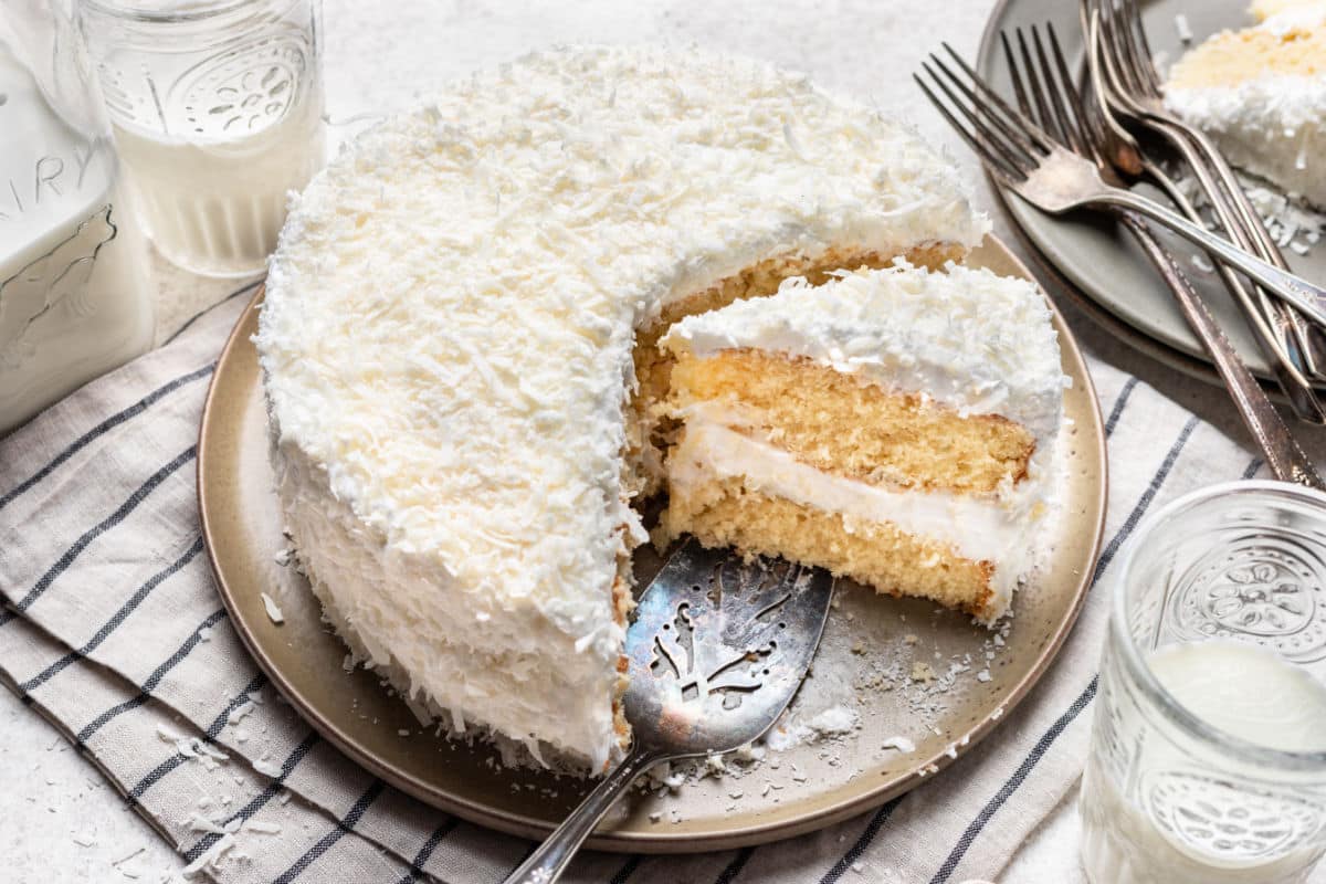 A coconut layer cake with a slice cut on a platter. 