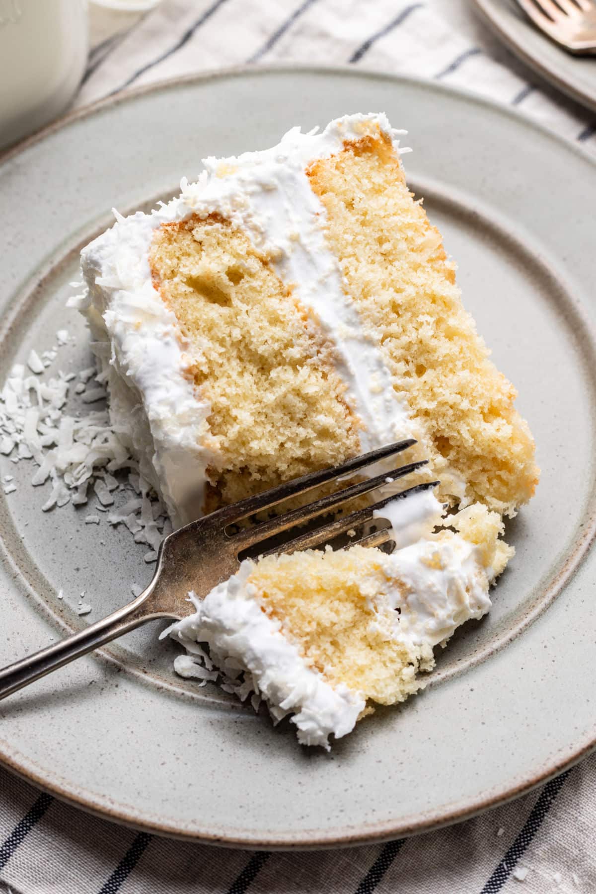 A fork taking a bite of a piece of coconut layer cake. 