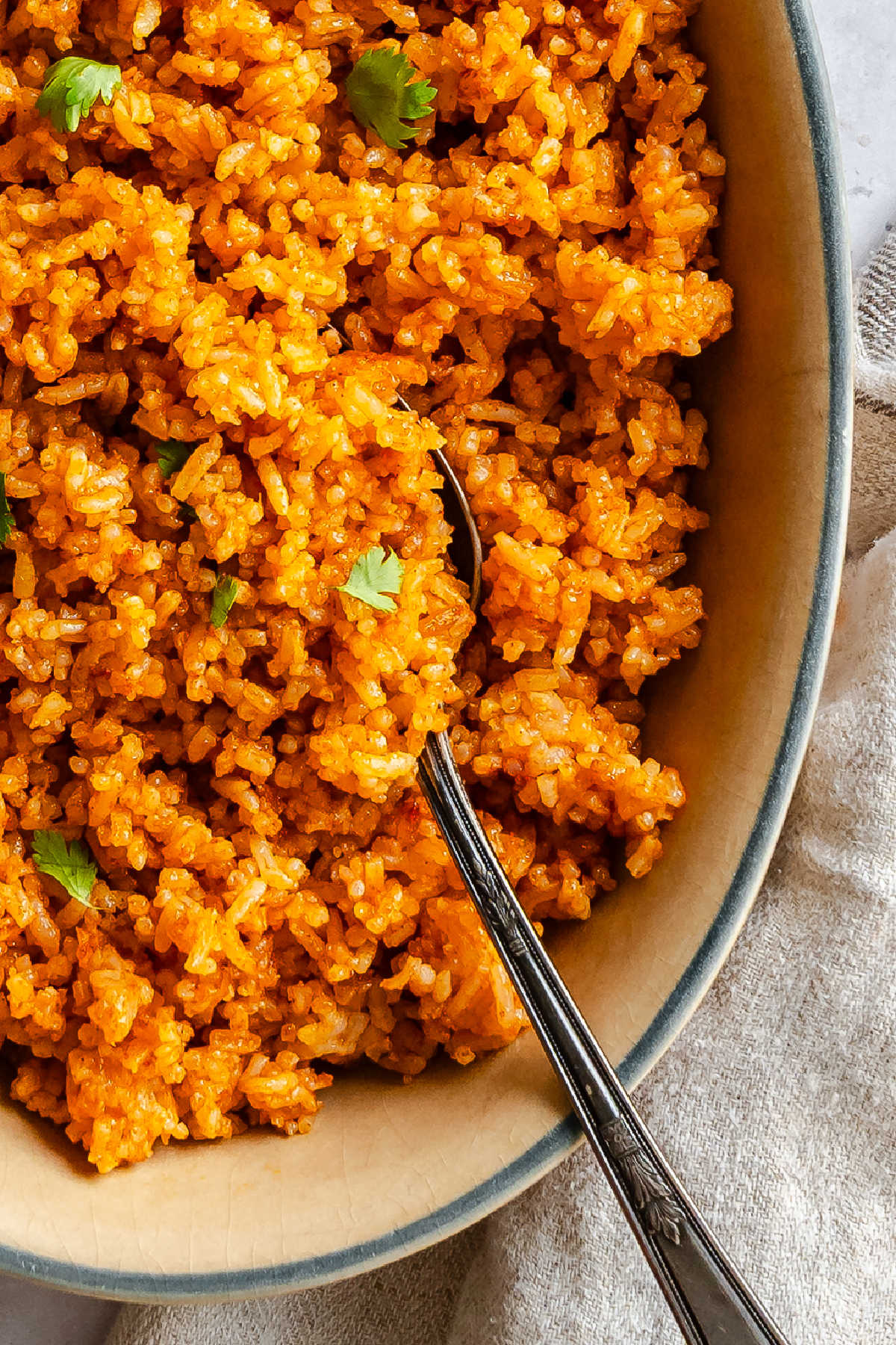 A dish of Mexican rice with a spoon in it next to a kitchen cloth.