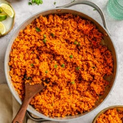 A skillet of Mexican rice next to fresh limes and cilantro.