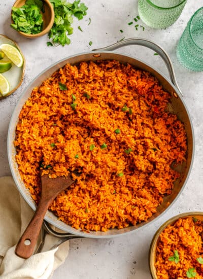 A skillet of Mexican rice next to fresh limes and cilantro.