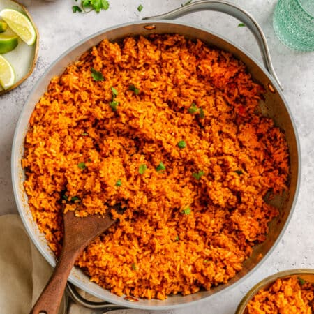 A skillet of Mexican rice next to fresh limes and cilantro.
