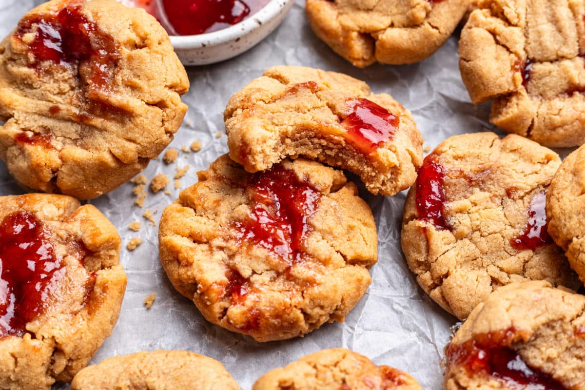Overlapping peanut butter and jelly cookies next to a dish of jam. 