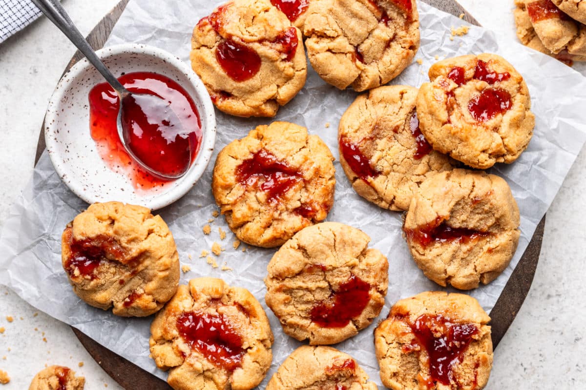 Peanut butter and jelly cookies on a piece of parchment paper next to a dish of jam.