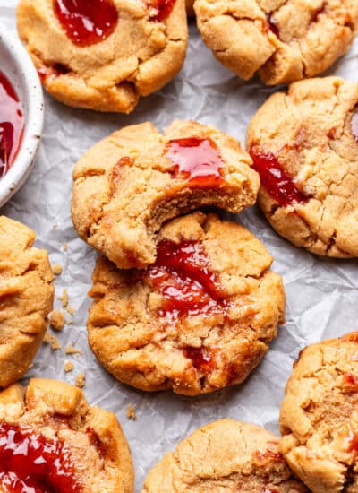A peanut butter and jelly cookie with a bite missing overlapping another cookies.