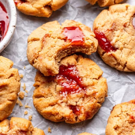 A peanut butter and jelly cookie with a bite missing overlapping another cookies.