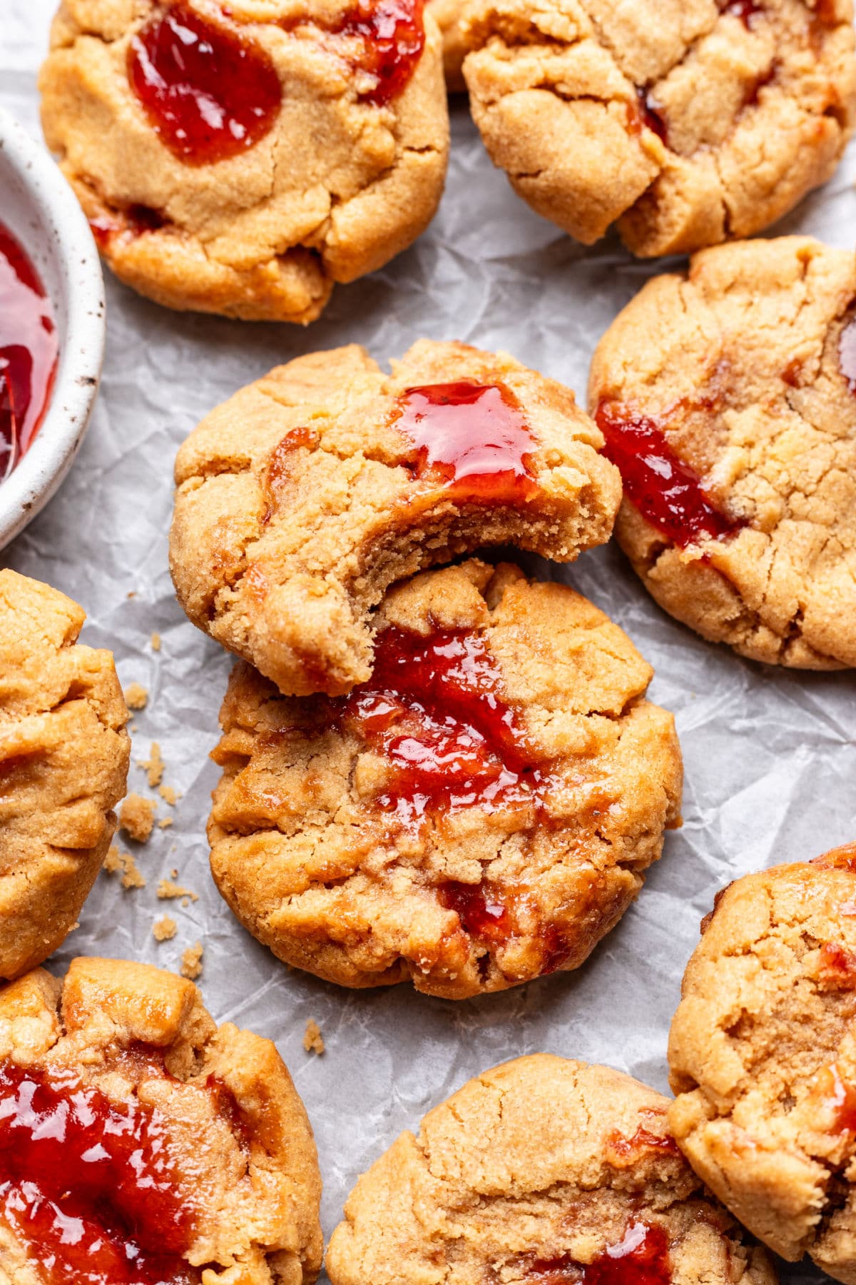 A peanut butter and jelly cookie with a bite missing overlapping another cookies.