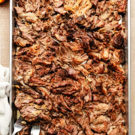A sheet pan of pork carnitas next to oranges and limes.