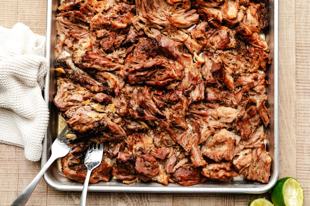 A tray of pork carnitas with two forks next to a kitchen cloth. 