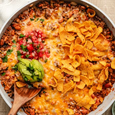 A taco skillet topped with corn chips, pico de gallo, and guac.