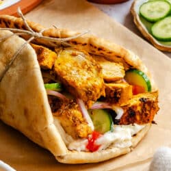 Chicken shawarma in a pita with toppings on brown parchment paper.