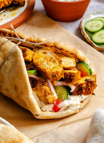 Chicken shawarma in a pita with toppings on brown parchment paper.