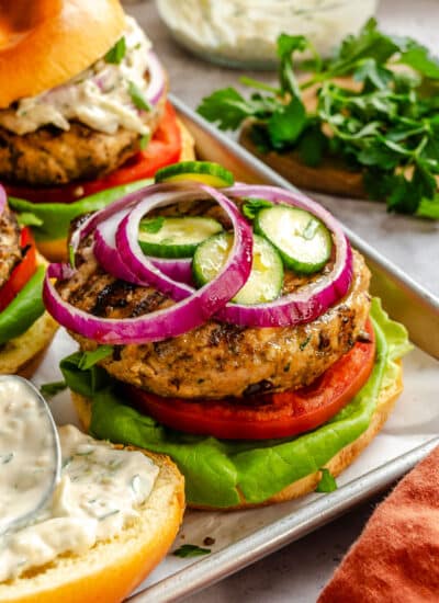 A Greek turkey burger topped with sliced cucumber and sliced red onion.
