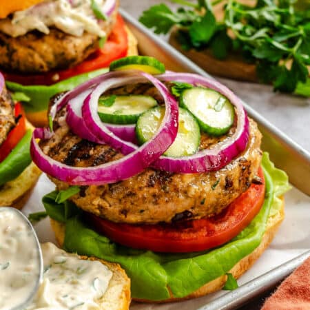 A Greek turkey burger topped with sliced cucumber and sliced red onion.