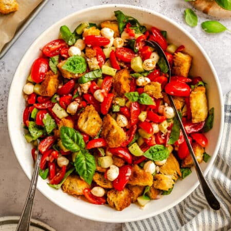 A bowl of panzanella salad next to a kitchen linen and a stack of plates.