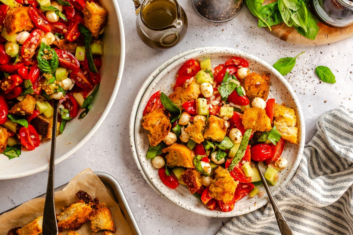 A plate of panzanella salad with a fork in it next to the dish of salad. 
