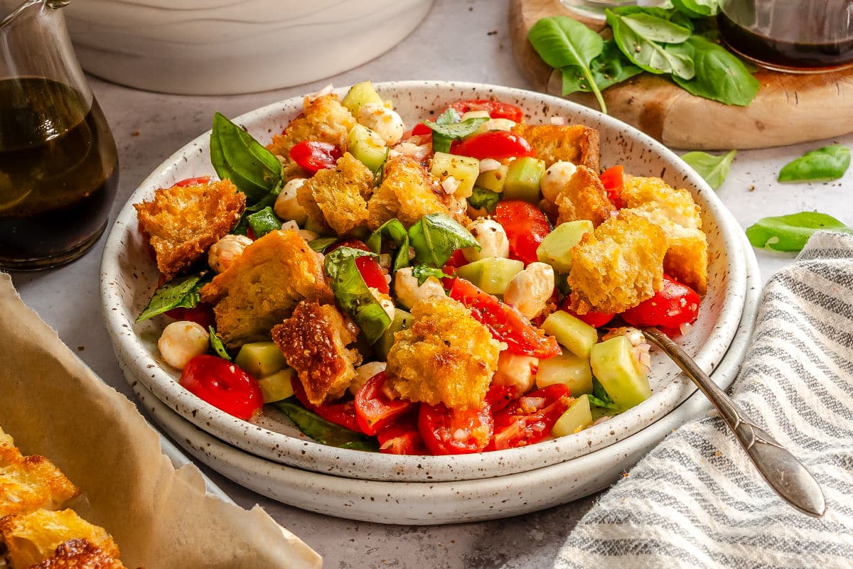 A dish of panzanella with a fork in it next to fresh basil leaves. 