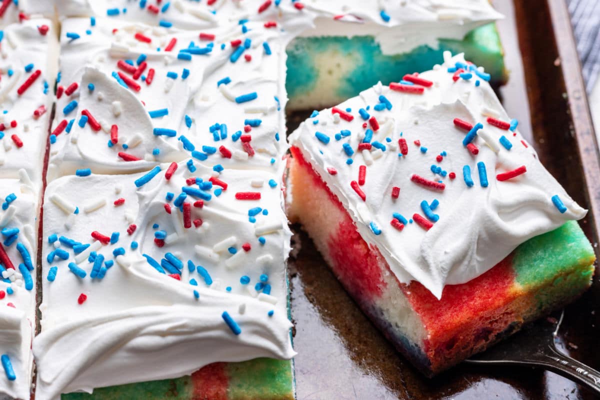 A slice of red white and blue poke cake at an angle next to the cake. 
