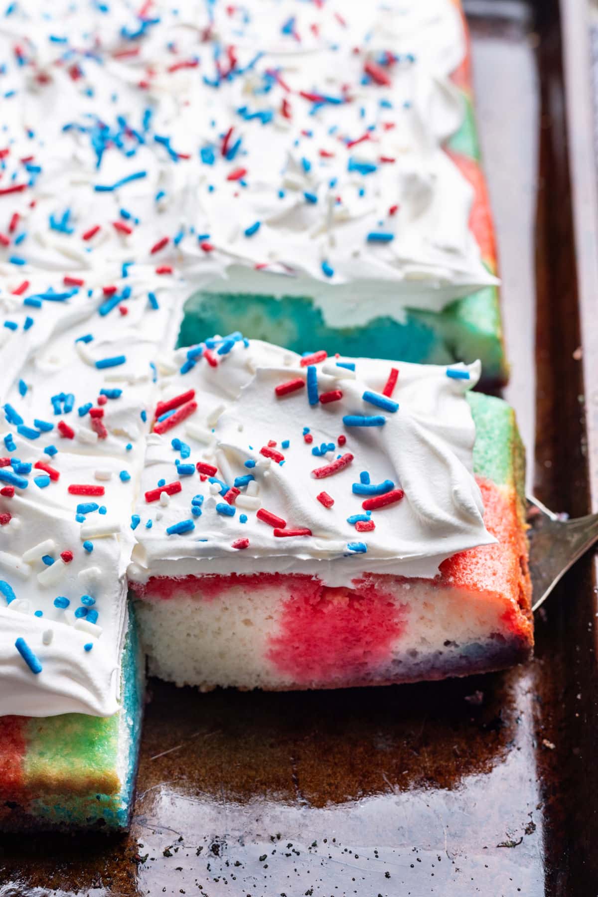 A cake server under a piece of red white and blue poke cake. 