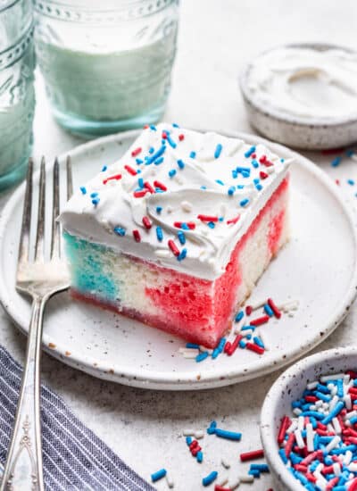 A slice of red white and blue poke cake on a plate next to a fork.