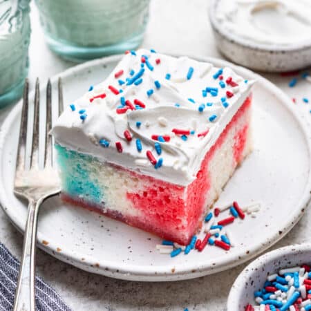 A slice of red white and blue poke cake on a plate next to a fork.