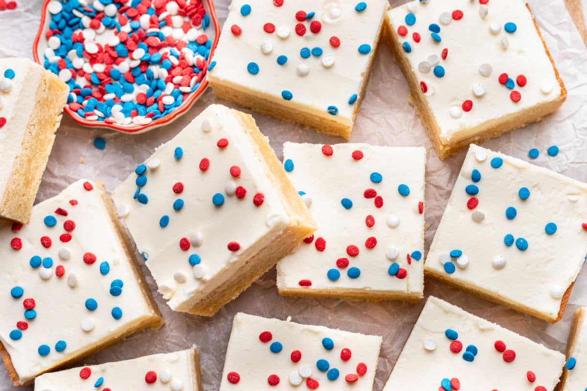 A sugar cookie bar topped with red white and blue sprinkles leaning against more bars. 