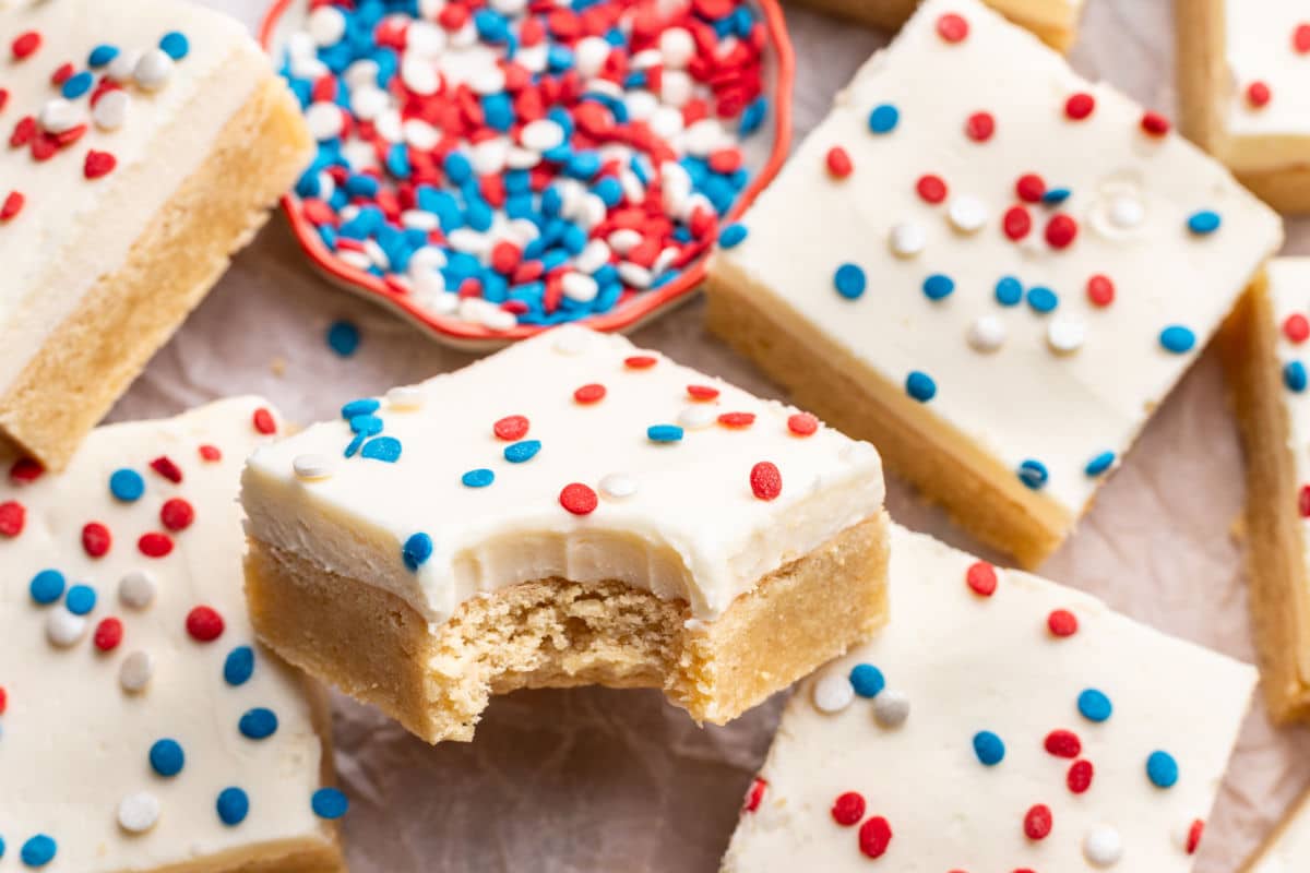 A sugar cookie bar with a bite missing topped with red white and blue sprinkles. 