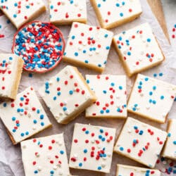 Overlapping red white and blue sugar cookie bars next to a dish of patriotic sprinkles.