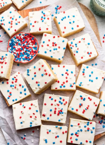 Overlapping red white and blue sugar cookie bars next to a dish of patriotic sprinkles.