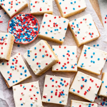 Overlapping red white and blue sugar cookie bars next to a dish of patriotic sprinkles.