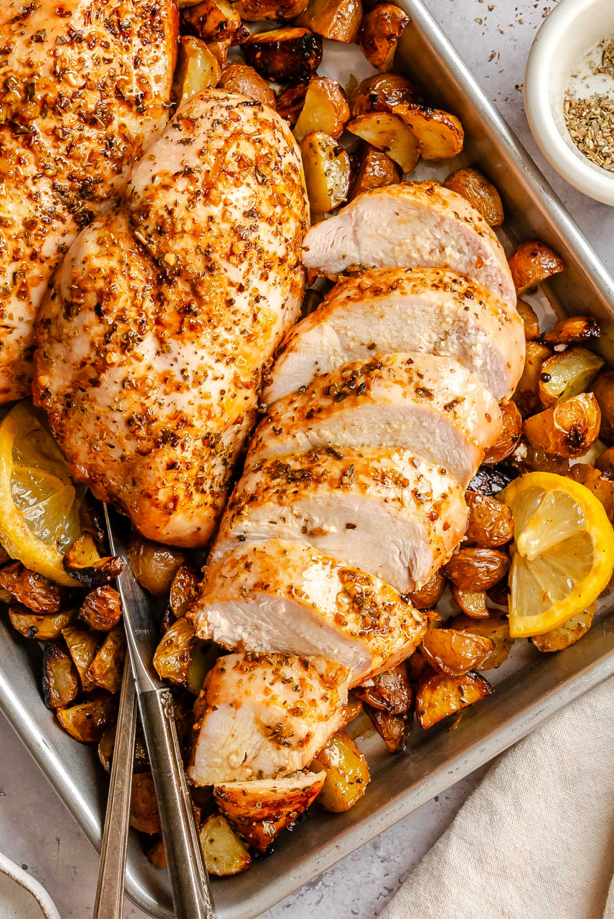 A sliced lemon garlic chicken breast on top of roast potatoes. 