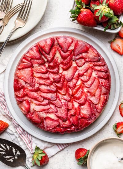 A strawberry upside-down cake on a platter next to a basket of fresh strawberries.