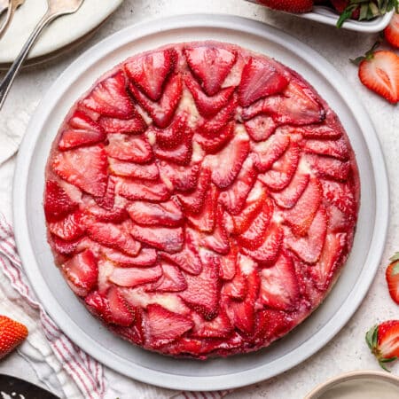 A strawberry upside-down cake on a platter next to a basket of fresh strawberries.