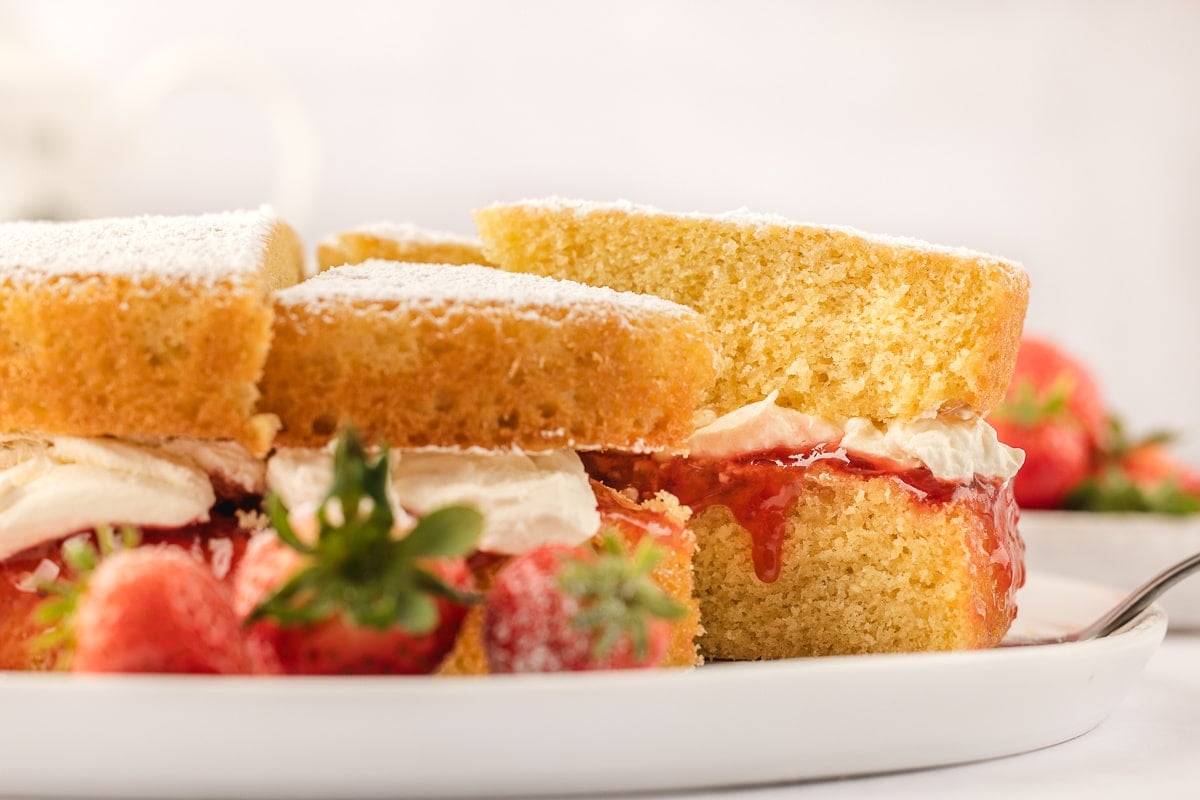 A cake server slightly removing a slice of Victoria sponge cake from the cake. 